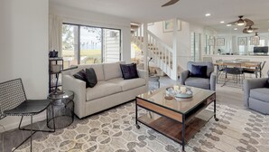 A spacious living room with a sofa, armchairs, a coffee table, and a dining area with a table and chairs. There are ceiling fans and a staircase leading to an upper level. - Beautiful villa with lake views and a floating dock!  271F (Miramar Beach)