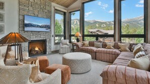 A spacious living room with a fireplace, large windows, a television, and a cozy seating area. - Lonestar Lodge: Sweeping Mountain Views, Hot Tub & Patio (Breckenridge)
