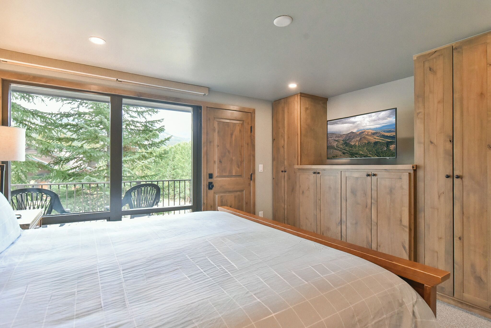 A bedroom with a large bed, wooden wardrobe, and a TV on the wall.