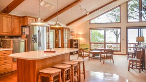 Una cocina amplia con armarios de madera, una isla grande con taburetes, un refrigerador y un comedor con sillas y una mesa.
