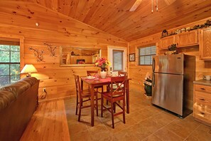 Interior de una cabaña de madera con una mesa de comedor, sillas, un sofá, un refrigerador y armarios de madera.