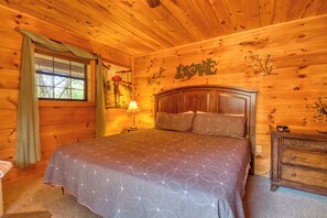 Een slaapkamer in een houten blokhut met een bed, nachtkastje, dressoir en raam met gordijnen.