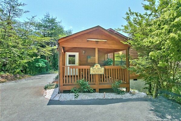A small cabin with a porch, surrounded by trees.