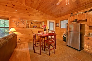 A wooden cabin interior with a dining table, chairs, a sofa, a refrigerator, and wooden cabinets. - Hot Tub | Wi-Fi | Pool Table (SEVIERVILLE)