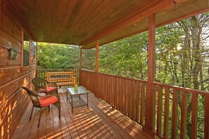 A wooden deck with a bench and a table, surrounded by a wooden railing, overlooking a forested area.