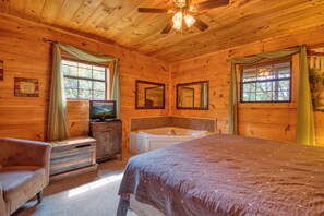 A wooden cabin bedroom with a bed, a vanity with a mirror, a bathtub, and a ceiling fan.