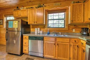 A wooden cabin kitchen with a refrigerator, dishwasher, wooden cabinets, a sink, and a window.
