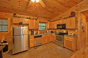 A wooden cabin kitchen with a refrigerator, stove, microwave, and wooden cabinets.