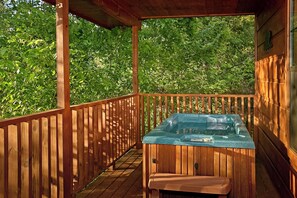 A wooden deck with a hot tub and a bench, surrounded by lush greenery.