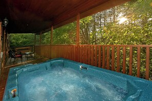 Een hottub onder een houten terras, met uitzicht op bomen en een bank.