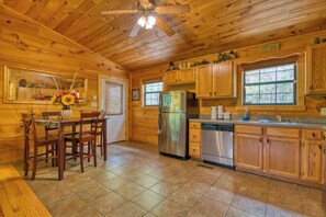A wooden cabin kitchen with a dining table, chairs, a refrigerator, a dishwasher, wooden cabinets, and a ceiling fan.