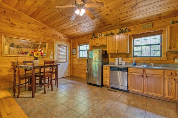 Cocina de cabaña de madera con mesa, sillas, refrigerador, lavavajillas, armarios de madera y ventilador de techo.