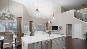 A spacious kitchen with a large island, modern pendant lights, and a dining area with wicker chairs. - 4BR Beach Villa w/ 6-Seater GOLF CART! Near Beach, Pool, Tram, Screened Porch (Miramar Beach)