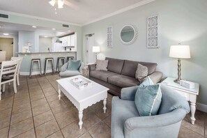 A living room with a sofa, armchairs, a coffee table, and a kitchen area in the background.