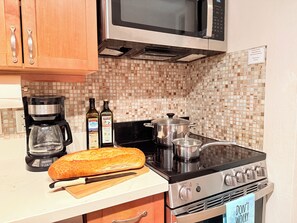 A kitchen with a stove, microwave, coffee maker, and bottles of olive oil.