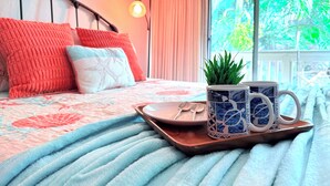 Una cama bien hecha con una colcha azul y blanca estampada, una bandeja con una taza y una cuchara, y una pequeña planta al lado.