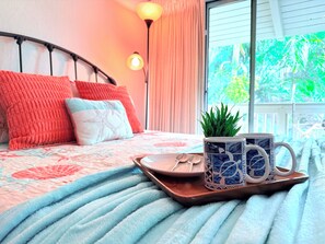 Un letto rifatto con una coperta a motivi blu e bianchi, un vassoio con una tazza e un cucchiaino, e una piccola pianta sul comodino.
