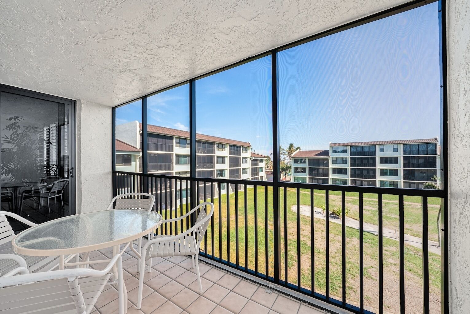 A balcony with a glass table and chairs, overlooking a building complex.