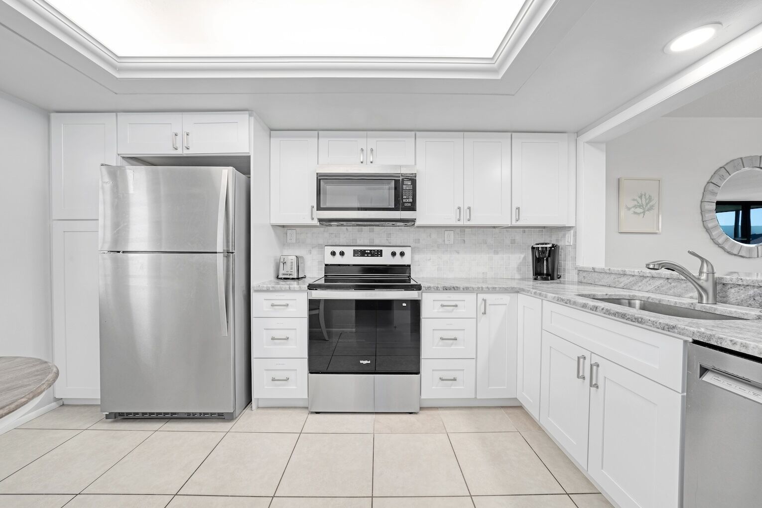 Una cocina moderna con armarios blancos, electrodomésticos de acero inoxidable, microondas integrado y un refrigerador grande.