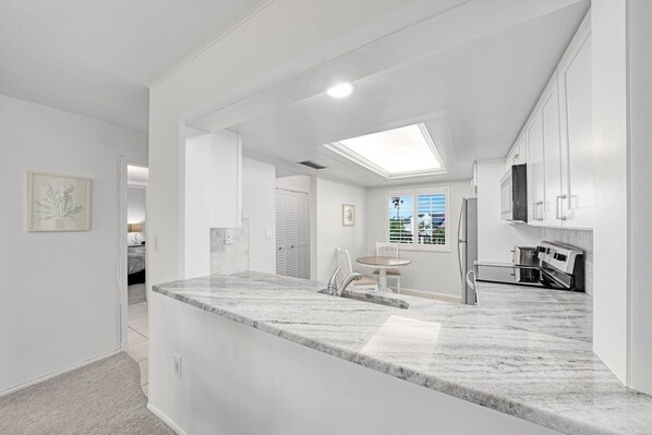 A modern kitchen with a marble countertop, stainless steel appliances, and a skylight.