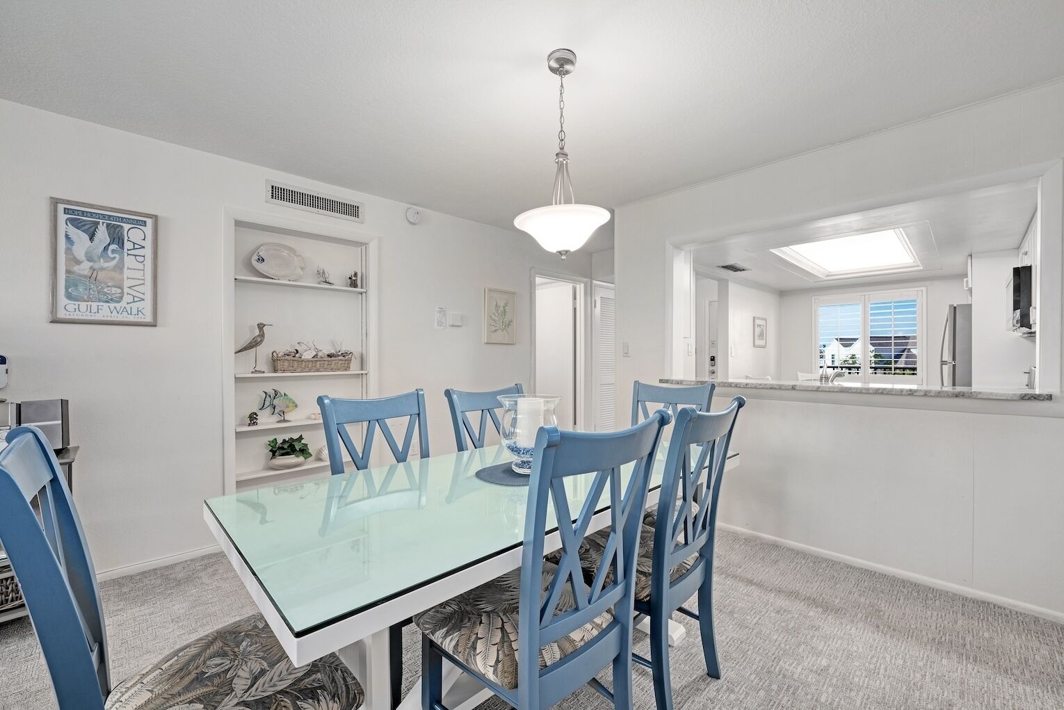 A dining area with a glass table and blue chairs, white walls, and a ceiling light.