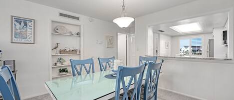 A dining area with a glass table and blue chairs, white walls, and a ceiling light.