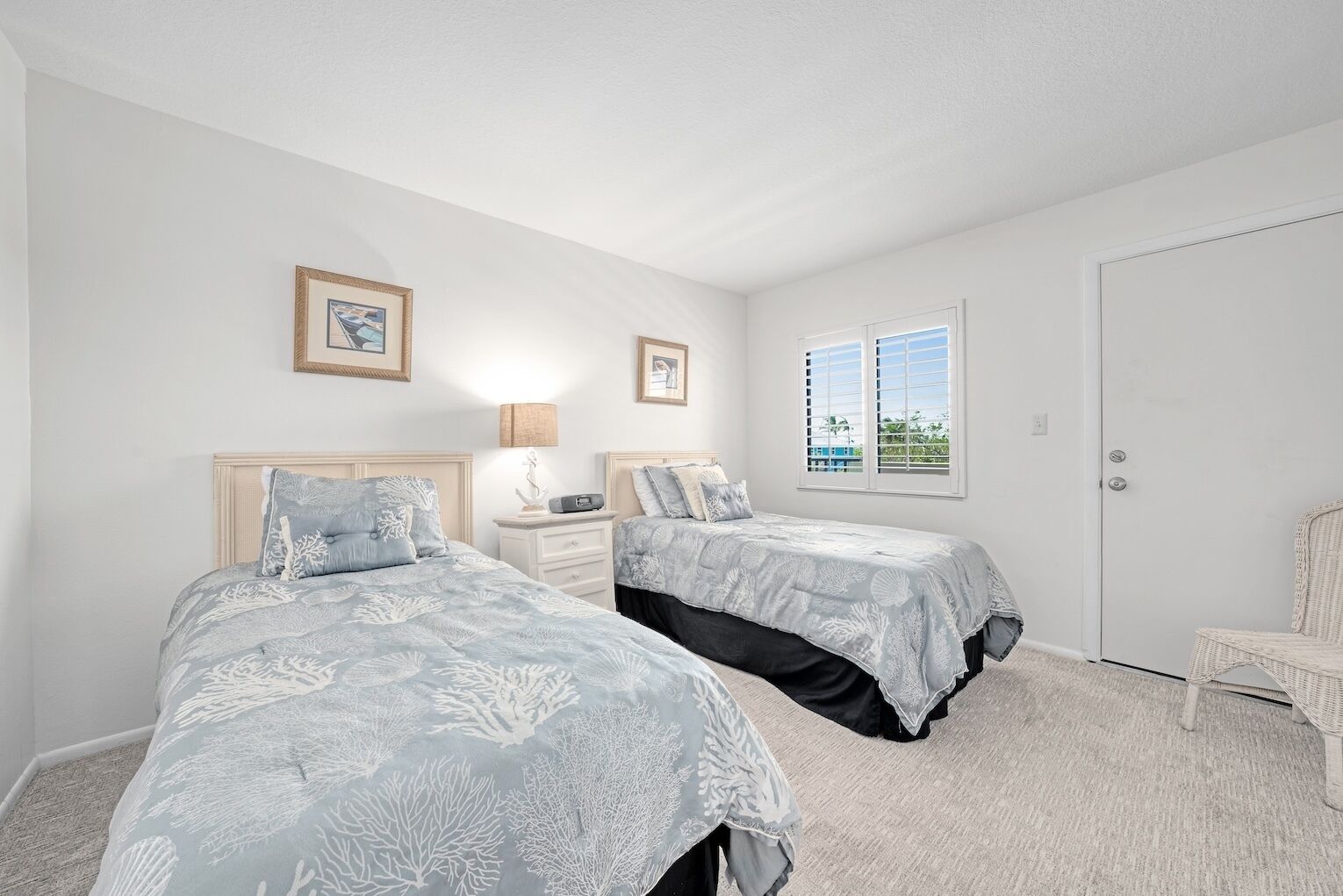 A bedroom with two beds, a nightstand, a lamp, a window, and a door.