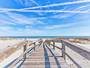 A wooden boardwalk leading to the beach with a clear sky and distant horizon.