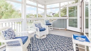 A covered porch with wicker chairs and a patterned floor, large windows, and a ceiling fan. - Three Sisters | Home with Pool, Patio, Two Porches (Tybee Island)