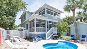 A two-story house with a swimming pool, outdoor seating, and a fenced yard. - Three Sisters | Home with Pool, Patio, Two Porches (Tybee Island)