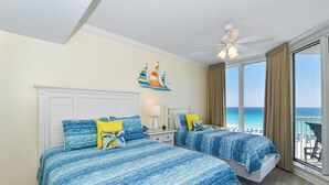 Habitación de hotel con dos camas, un ventilador de techo, un ventanal con vista a la playa y una decoración náutica en la pared.