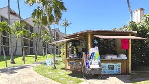 Quiosco en la playa con equipo de alquiler para actividades acuáticas, rodeado de palmeras y un edificio con balcones.