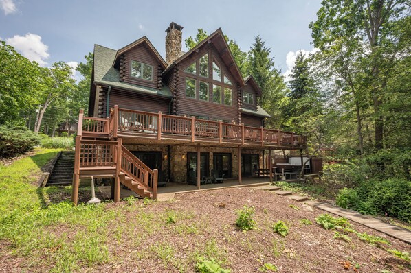 A log cabin with a covered porch, stone chimney, and a wooden staircase leading to the entrance.