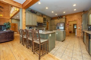 A spacious kitchen with wooden cabinets, a central island with bar stools, and a large window providing natural light. - Luxury Log Chalet w/ Pool & Fireplace (Oakland)