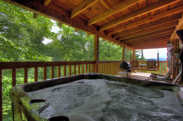 A hot tub with a wooden deck and a view of lush greenery.