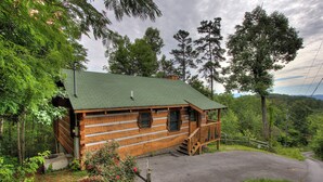 A log cabin with a green roof, wooden exterior, and a porch with steps leading to a door.