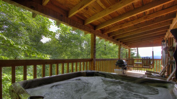 A hot tub with a wooden deck and a view of lush greenery.