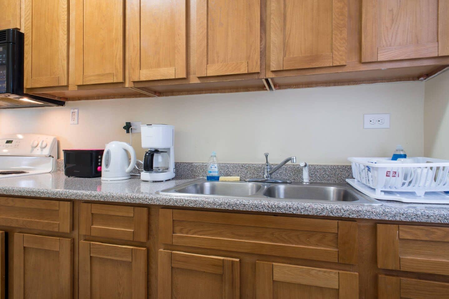 A kitchen with wooden cabinets, a stainless steel sink, a coffee maker, and a toaster.