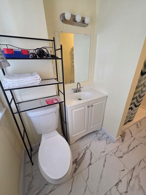 A bathroom with a toilet, a sink, a mirror, and a shelf with towels. - Salem Spacious First Floor 3-4BR! (Salem)