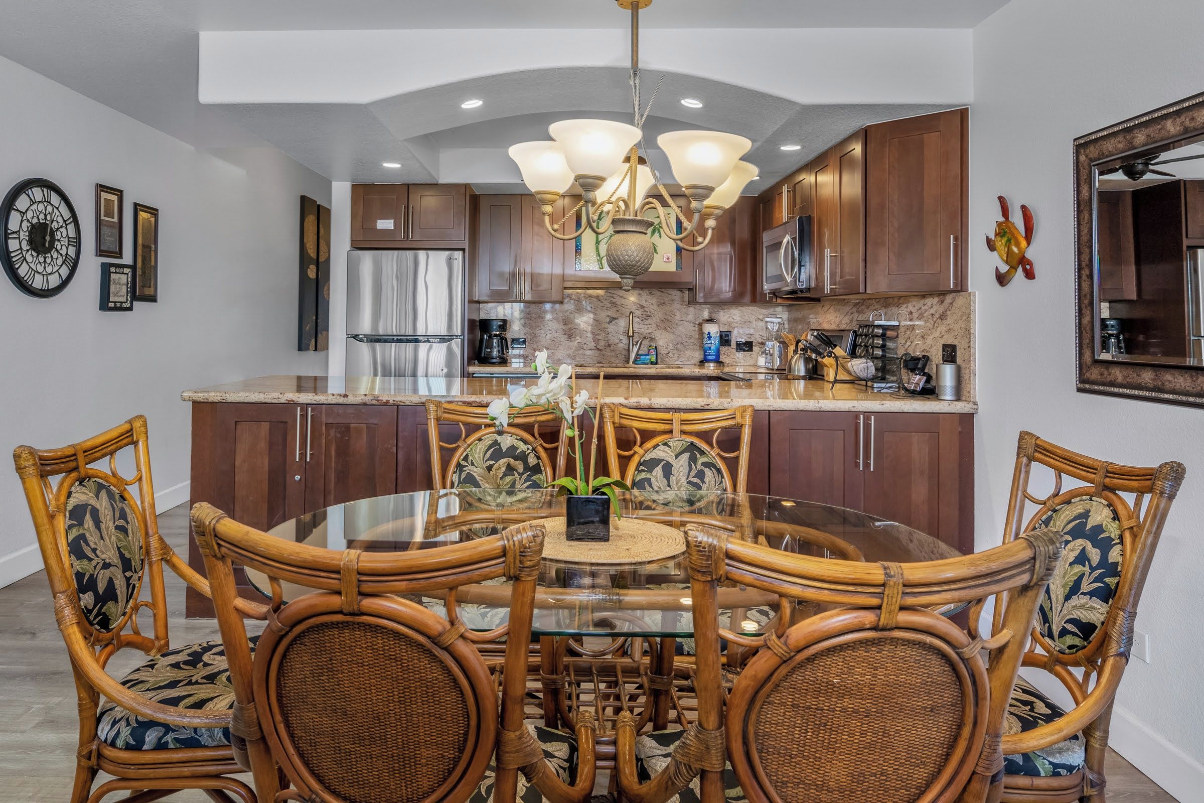 A modern kitchen with dark wood cabinets, stainless steel appliances, and a round dining table surrounded by wicker chairs.