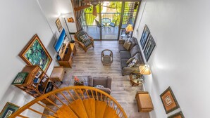 A spacious living area with a wooden spiral staircase, a sofa set, a dining table, and a balcony with outdoor seating.