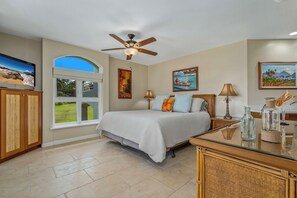 A bedroom with a bed, a ceiling fan, a TV, and a window with a view of the outdoors.