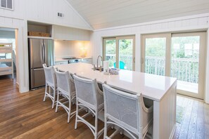 A modern kitchen with a large island, white wicker chairs, and a view of a wooden deck. - Watervale - Gulf View, Pool, Gulf Trace neighborhood Grayton Beach! (Santa Rosa Beach)