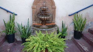 Eine Steinfountain mit Blumendekor, begleitet von Kübelpflanzen und einem blauen Geländer.