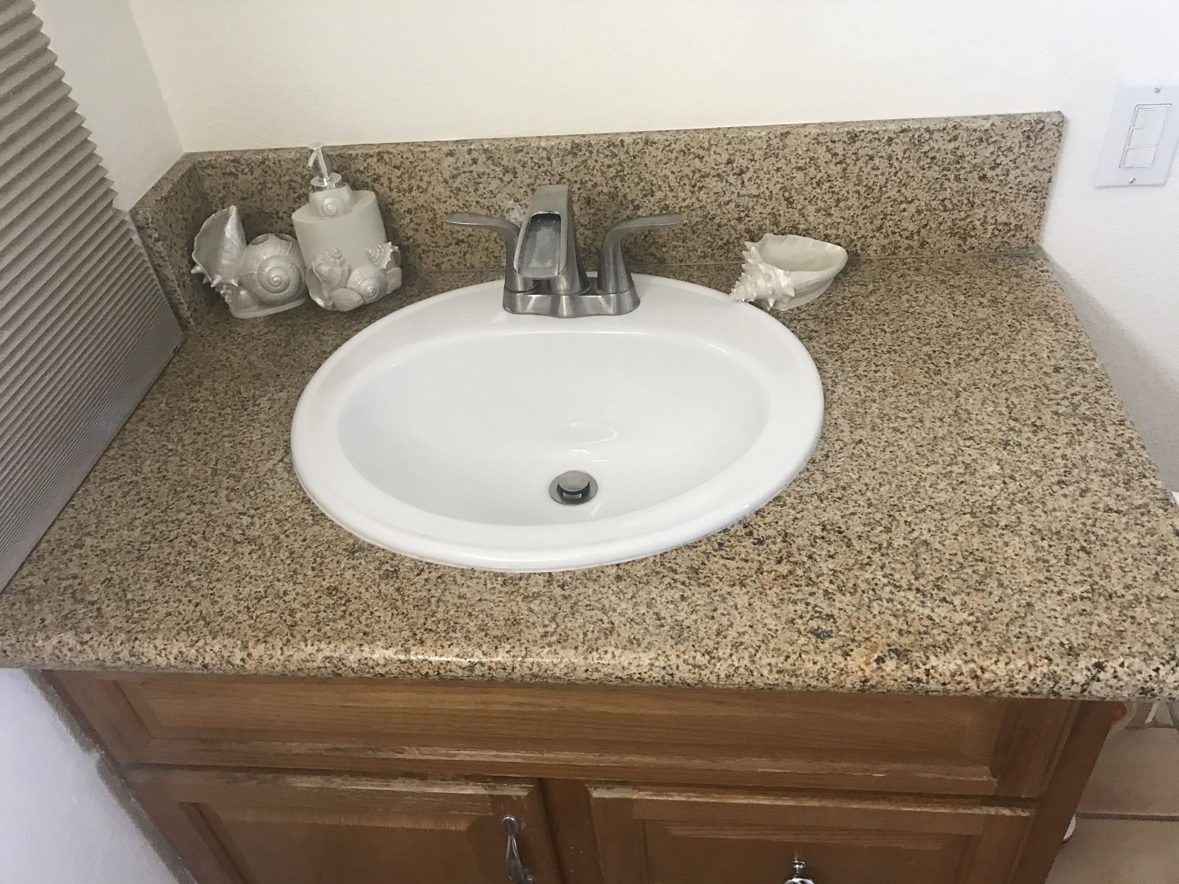 A bathroom with a white sink, granite countertop, and wooden cabinets.