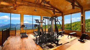Ein Fitnessstudio mit Trainingsgeräten und großen Fenstern mit Blick auf eine gebirgige Landschaft.