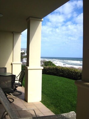 A patio with a view of the ocean, a table with chairs, and a well-maintained lawn. - Gulf front condo, 1st floor- walk out to beach, Pool, Santa Rosa beach (Santa Rosa Beach)