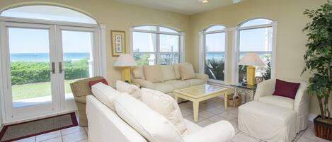 A spacious living room with a large window overlooking the ocean, a ceiling fan, and a potted plant.