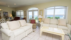 A spacious living room with two cream-colored sofas, a small table, and a view of the outdoors through large windows. - Gulf front condo, 1st floor- walk out to beach, Pool, Santa Rosa beach (Santa Rosa Beach)