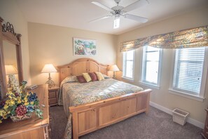 A bedroom with a wooden bed, two bedside lamps, a ceiling fan, a window with blinds, and a floral-patterned curtain. - Gulf front condo, 1st floor- walk out to beach, Pool, Santa Rosa beach (Santa Rosa Beach)